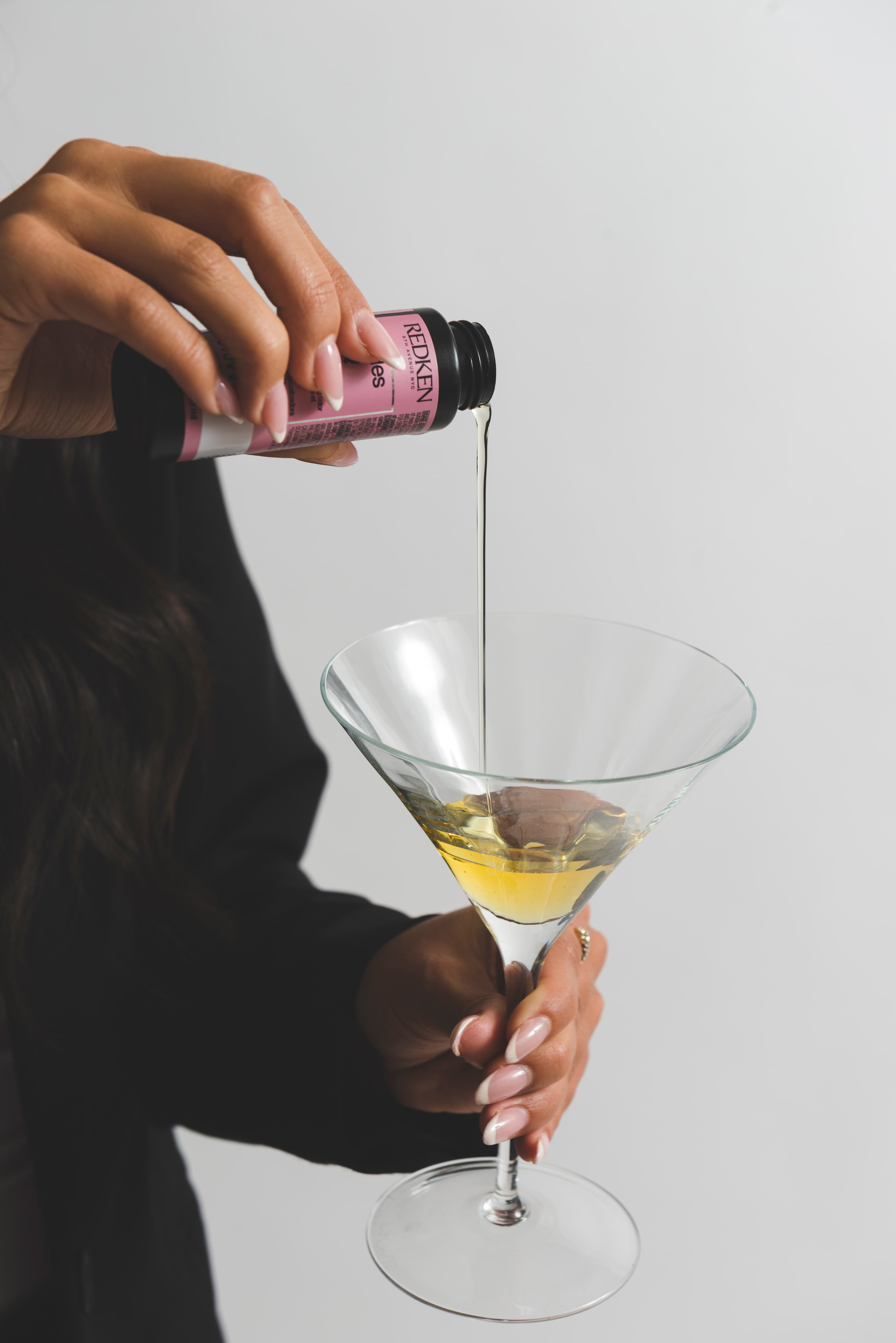Close-up of hair color being poured from a bottle into a stemmed glass.